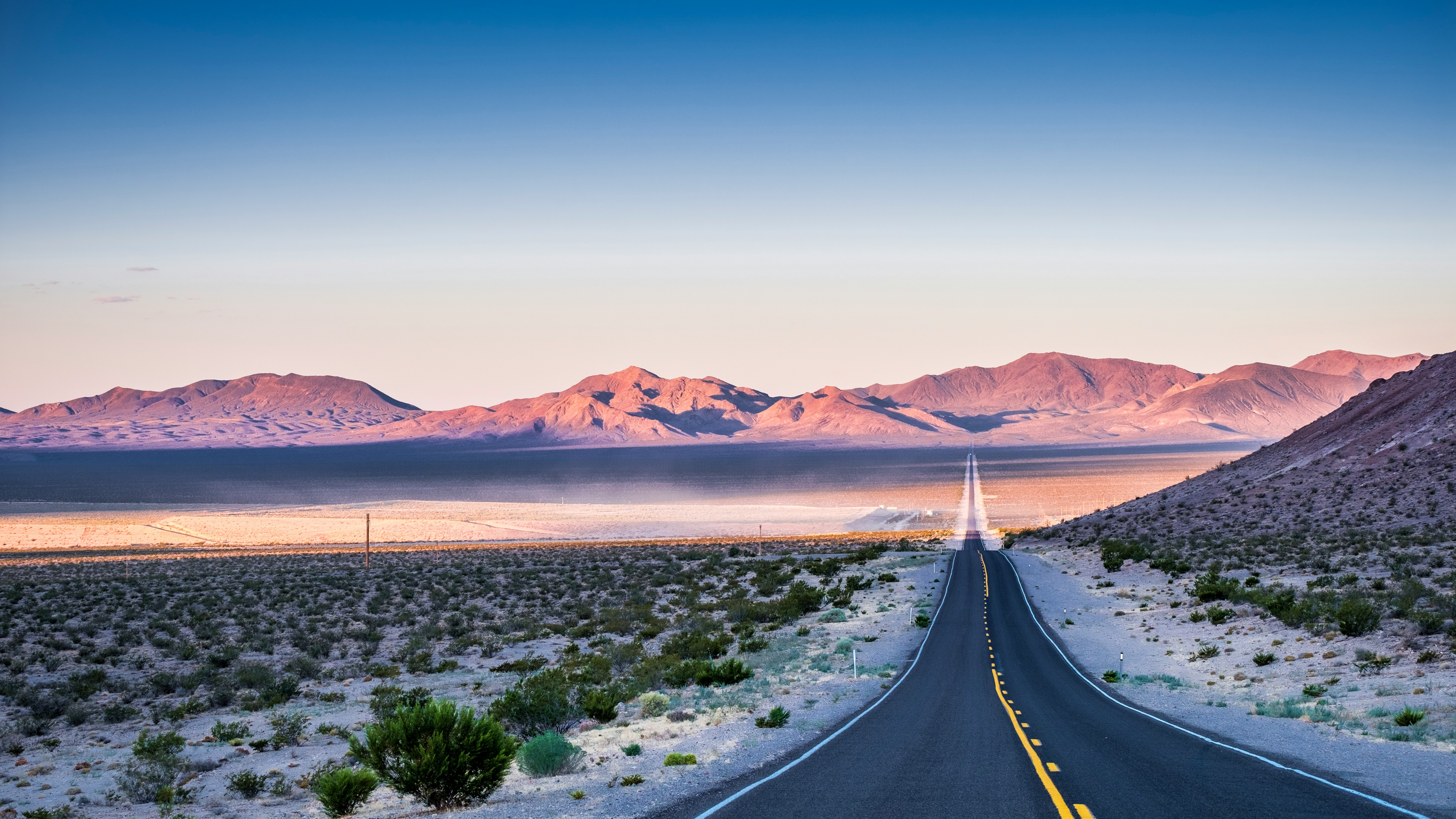 An open road stretching across the desert toward distant mountains at first light
